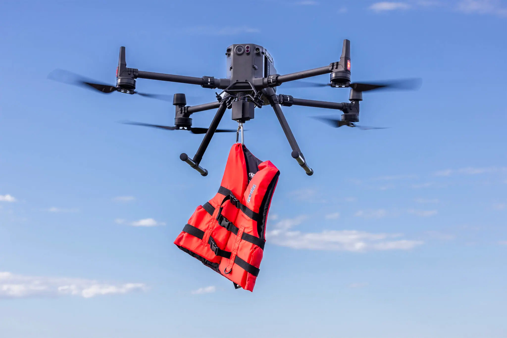 A black drone hangs an orange life jacket in mid-air
