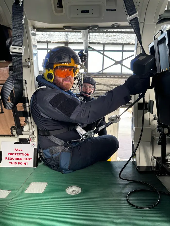 A man wearing a black shirt and an orange hat sits on top of a helicopter