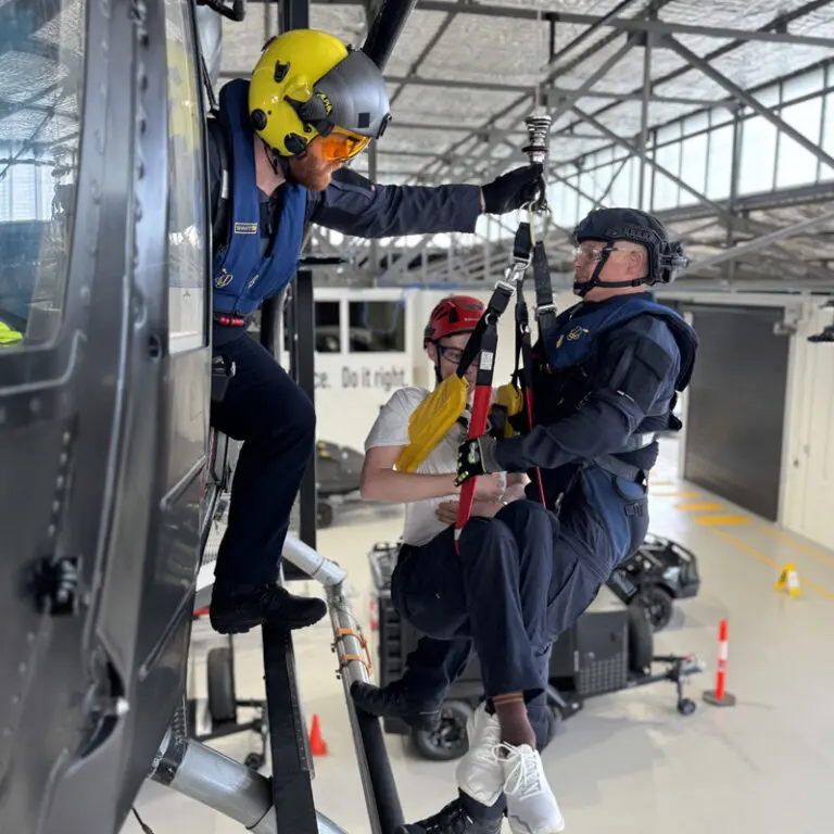 A man dressed in black carries a woman in white as they descend by rope from a black helicopter