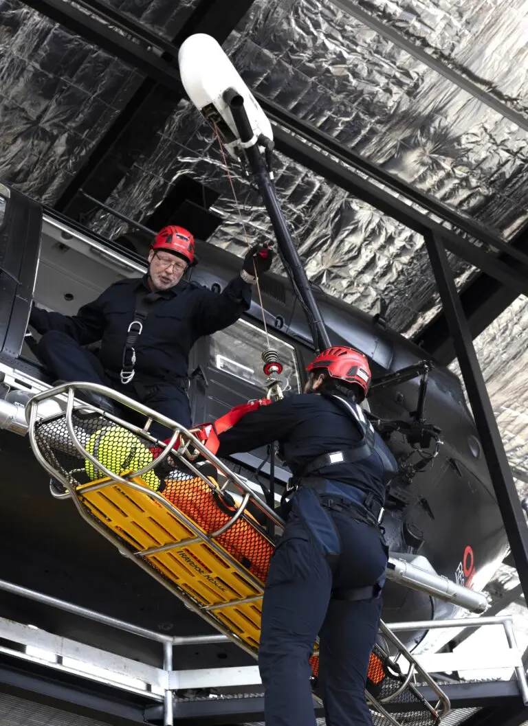 A man dressed in black is descending from a black helicopter carrying a field stretcher
