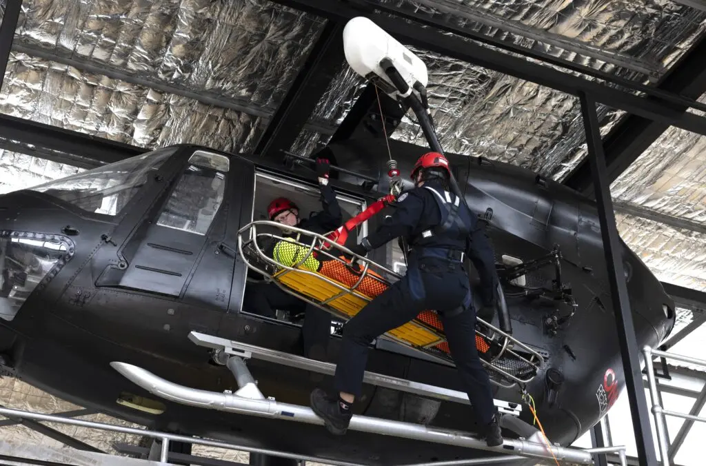 A man dressed in black is descending from a black helicopter carrying a field stretcher