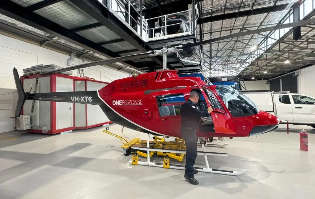 A man wearing a black shirt is examining a red and black helicopter