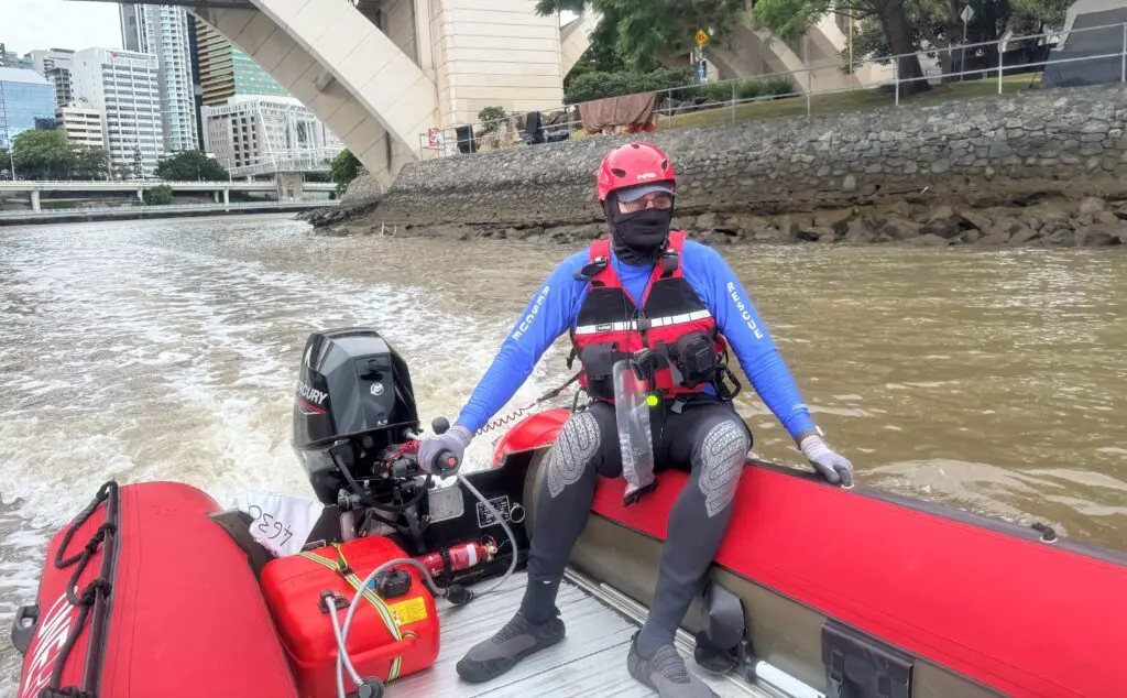 A man in a blue shirt, red vest, and red hat is piloting a red inflatable boat