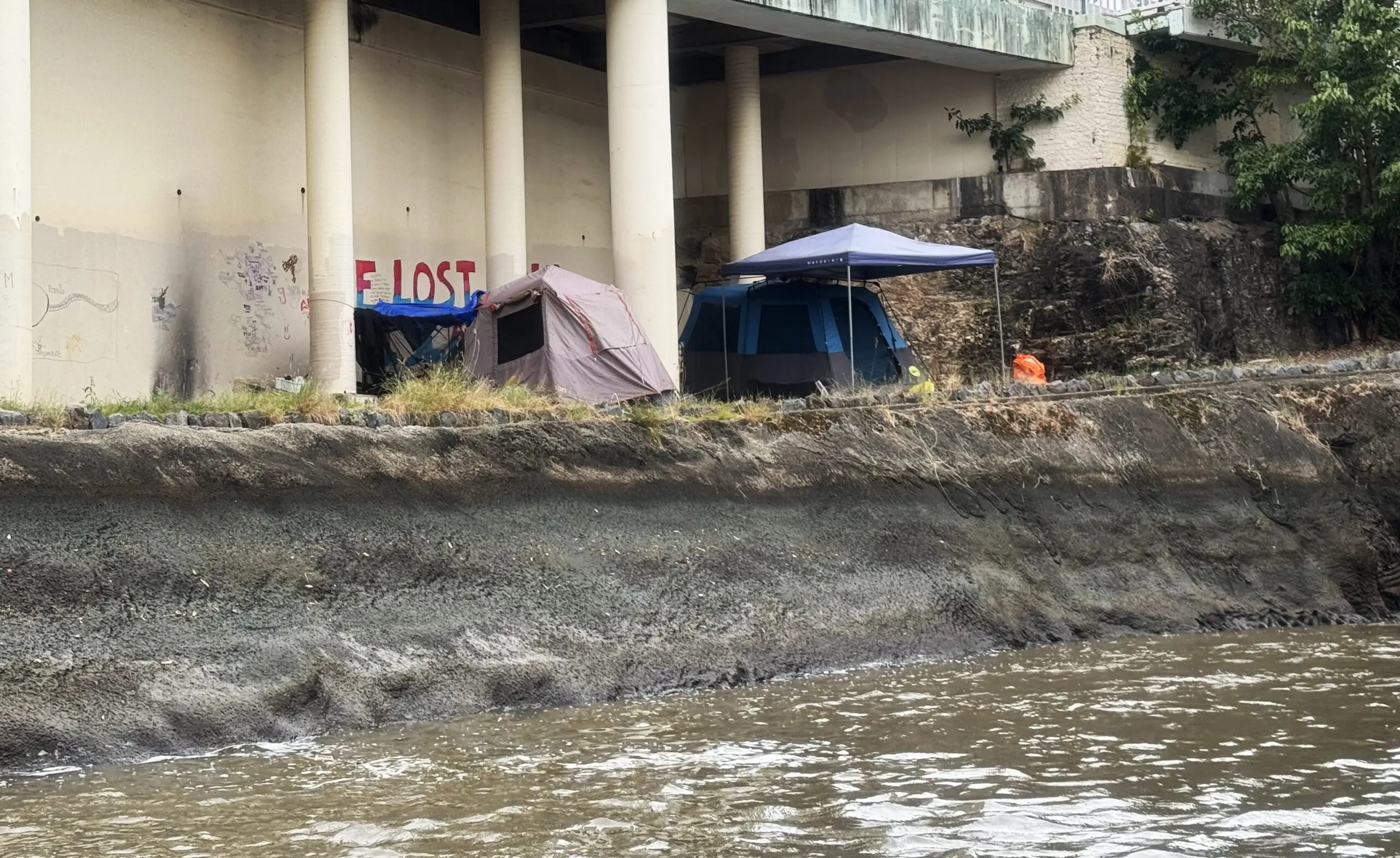 Three tents stand along the edge of the river