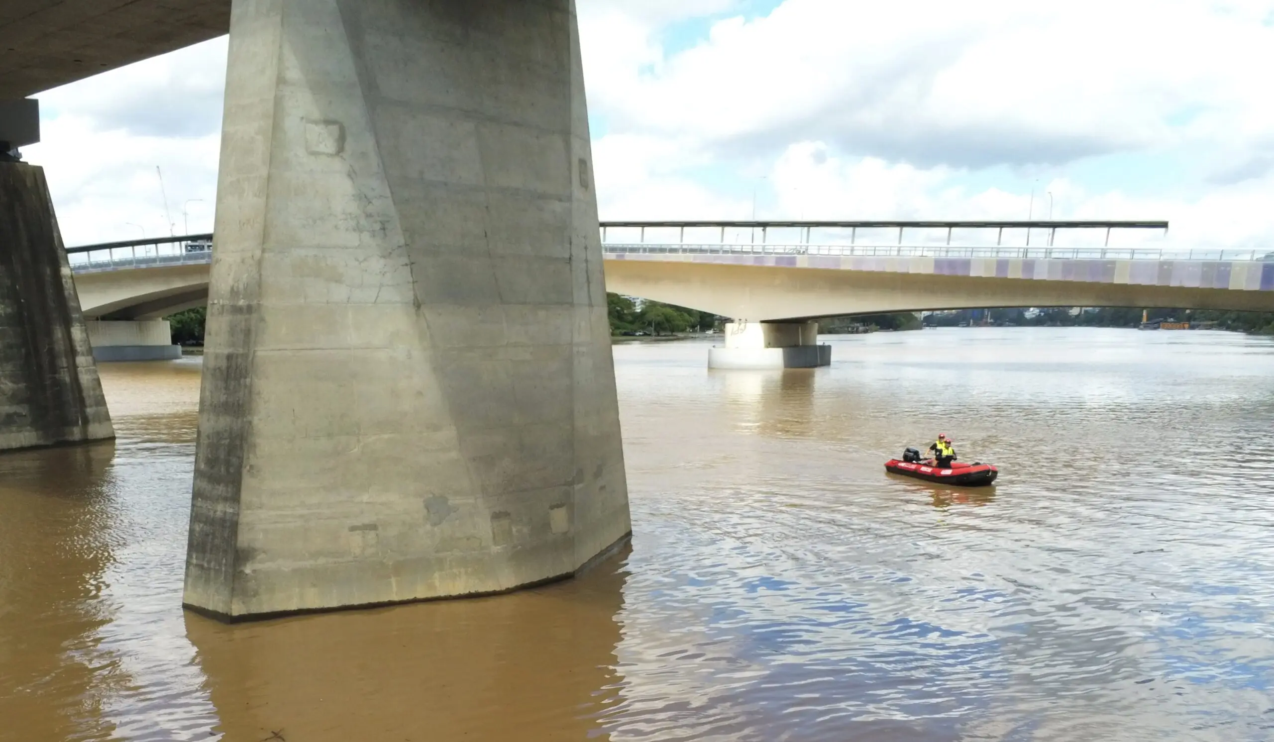 A red inflatable boat moves through the river beneath a bridge