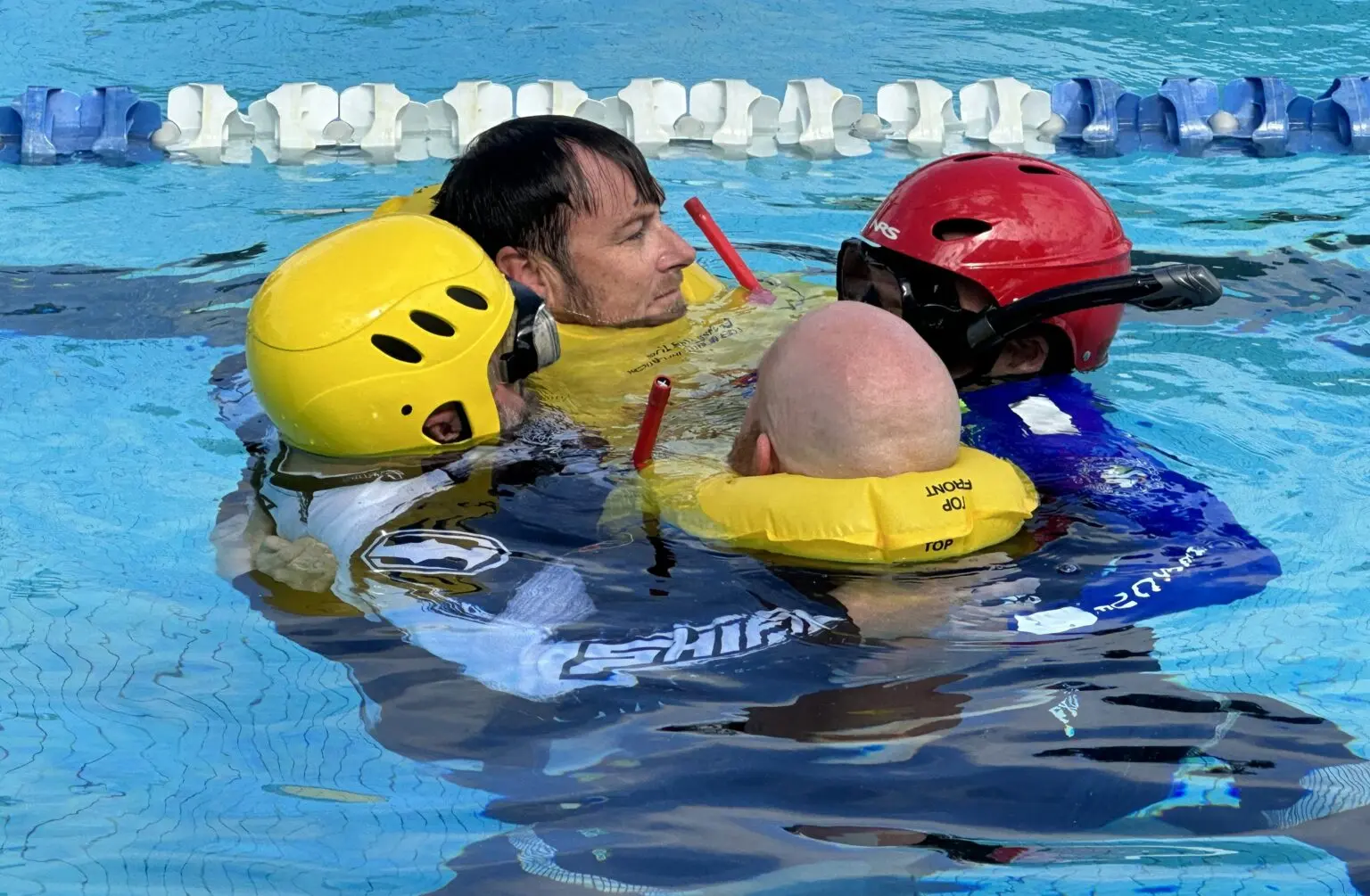 Three men are assisting another man in the center of a pool
