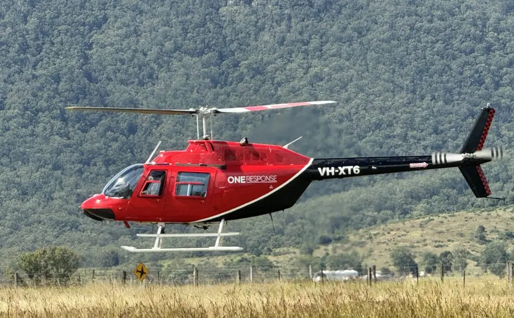 A red and black helicopter is descending to land in the middle of the forest