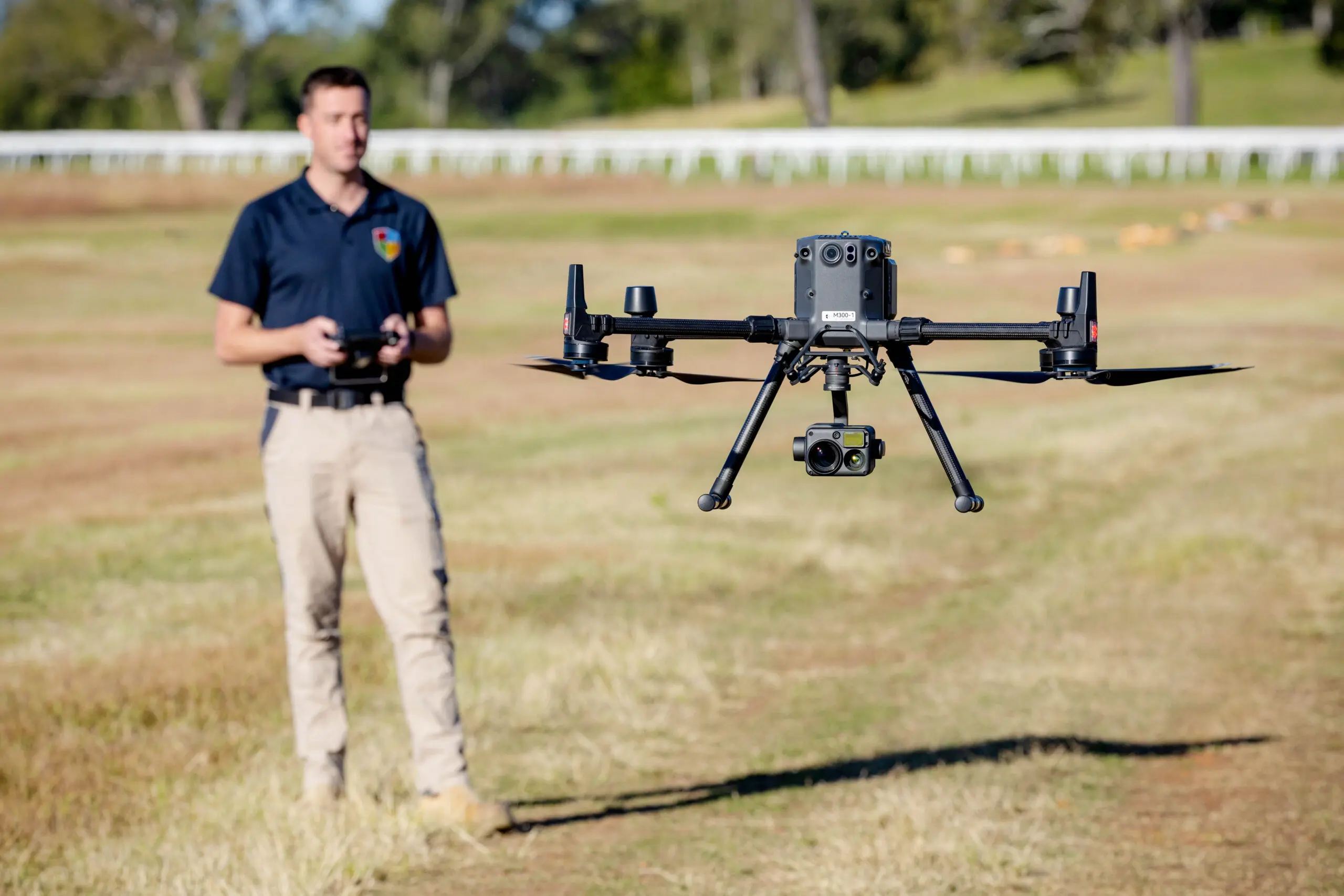 A man wearing a black shirt operates a black drone in the center of a field
